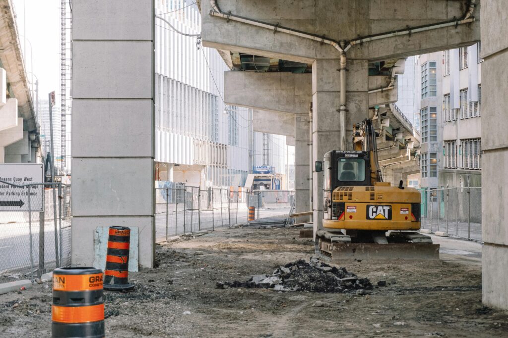 Site of roadway under concrete bridge construction with heavy equipment on dirty ground