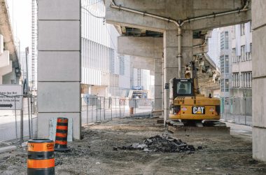 Site of roadway under concrete bridge construction with heavy equipment on dirty ground