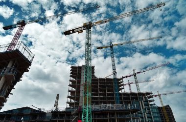 Urban construction site with numerous cranes framing rising skyscrapers against a blue sky.